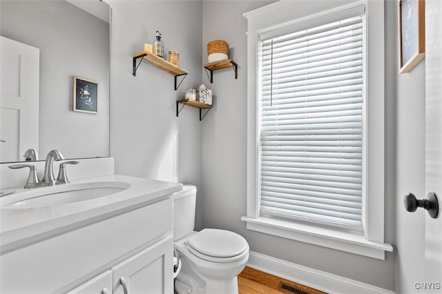 bathroom with baseboards, toilet, a healthy amount of sunlight, and vanity