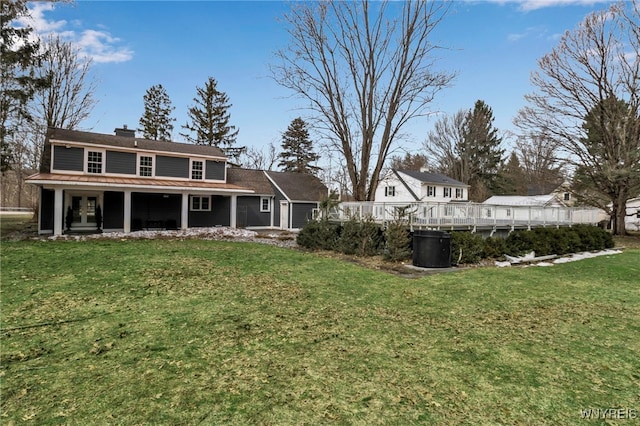 rear view of house with a wooden deck, a chimney, and a yard