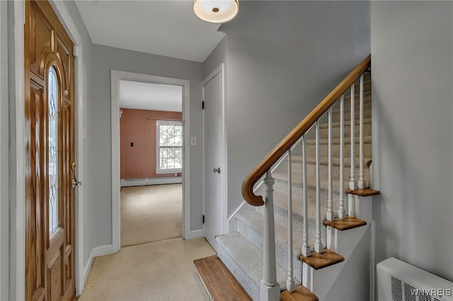 foyer entrance featuring a baseboard heating unit, baseboards, light colored carpet, and stairs