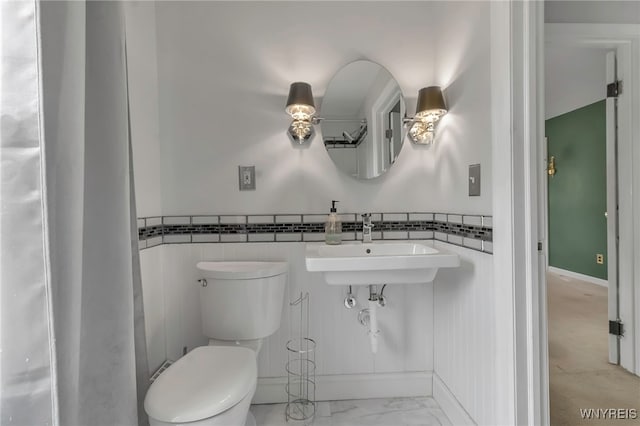 bathroom featuring toilet, a wainscoted wall, marble finish floor, and a sink