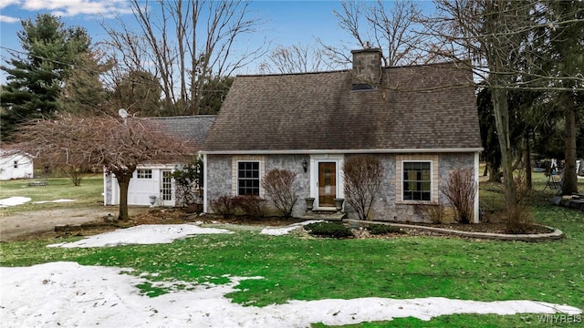 view of front facade featuring a front yard, stone siding, roof with shingles, and a chimney