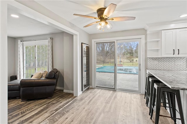 dining room featuring light wood finished floors, a healthy amount of sunlight, a ceiling fan, and baseboards