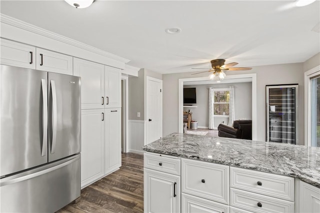 kitchen featuring a wainscoted wall, light stone counters, dark wood finished floors, white cabinetry, and freestanding refrigerator