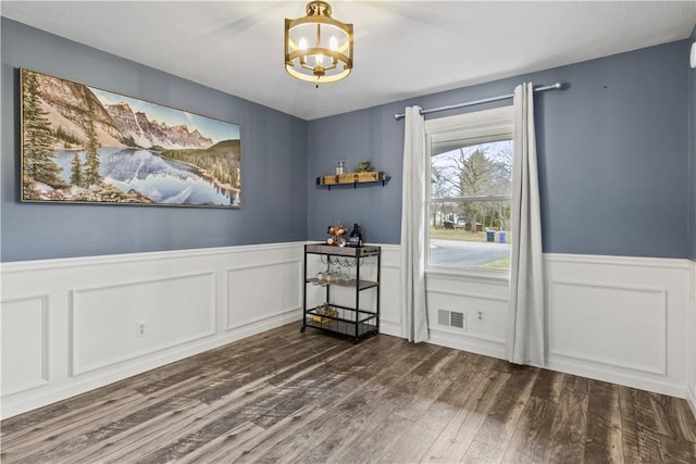 dining space with a wainscoted wall, visible vents, an inviting chandelier, and wood finished floors