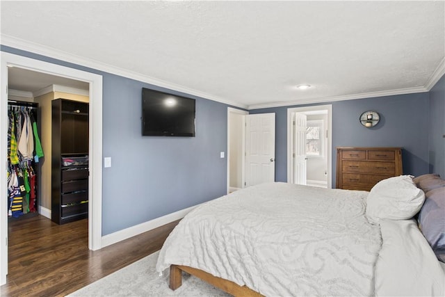 bedroom featuring a walk in closet, ornamental molding, wood finished floors, a closet, and baseboards