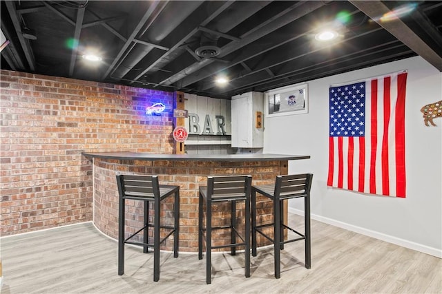 bar with baseboards, wood finished floors, a dry bar, and brick wall