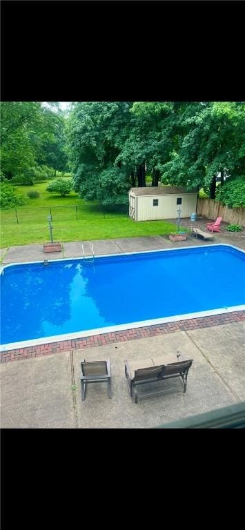 outdoor pool featuring fence, an outdoor structure, a patio area, a storage shed, and a lawn