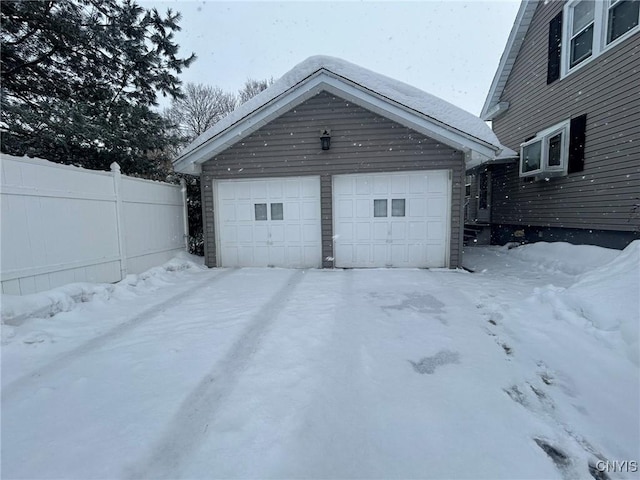 snow covered garage featuring fence