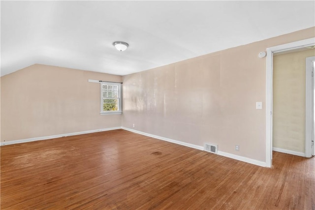 spare room with vaulted ceiling, wood finished floors, visible vents, and baseboards