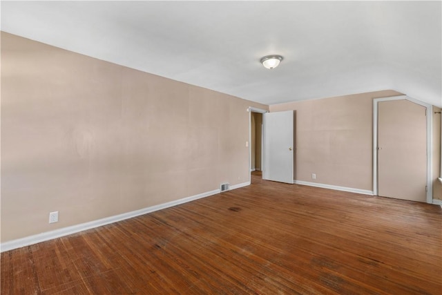 interior space with vaulted ceiling, visible vents, baseboards, and hardwood / wood-style flooring