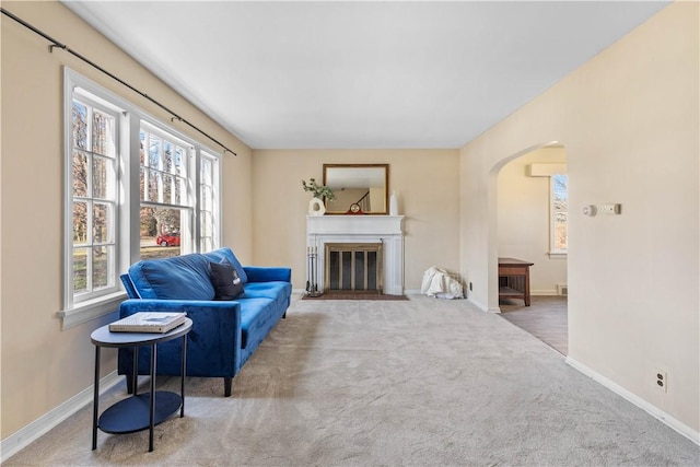 living area featuring carpet flooring, a fireplace with flush hearth, baseboards, and arched walkways