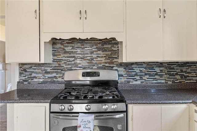 kitchen with tasteful backsplash, stainless steel range with gas stovetop, white cabinetry, and dark countertops