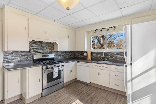 kitchen featuring dark countertops, decorative backsplash, white appliances, and a sink