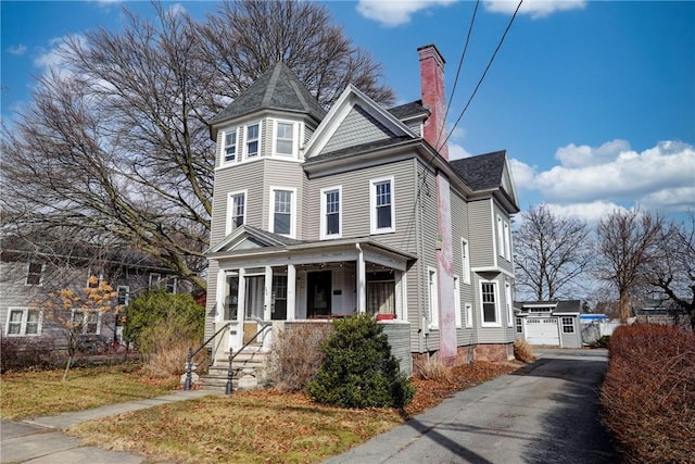 victorian house with a detached garage, covered porch, and a chimney