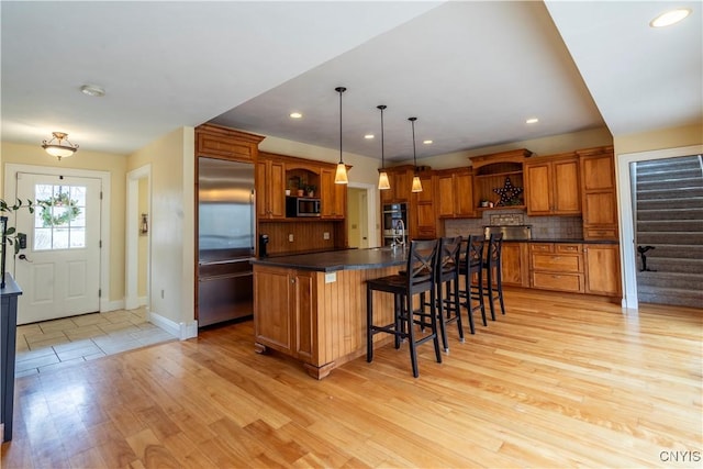 kitchen with brown cabinetry, open shelves, stainless steel appliances, decorative backsplash, and dark countertops