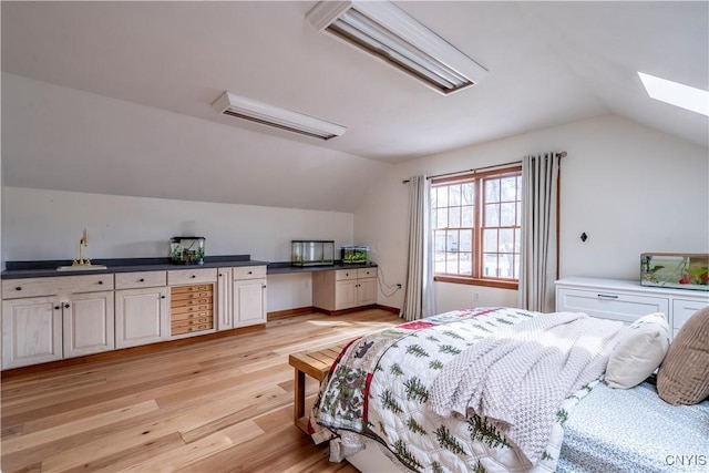 bedroom with lofted ceiling with skylight, light wood-style flooring, and a sink