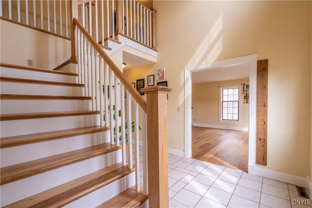 stairs with tile patterned floors, visible vents, baseboards, and a high ceiling