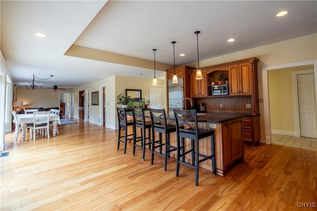 kitchen with light wood-type flooring, stainless steel microwave, a kitchen breakfast bar, open floor plan, and brown cabinetry