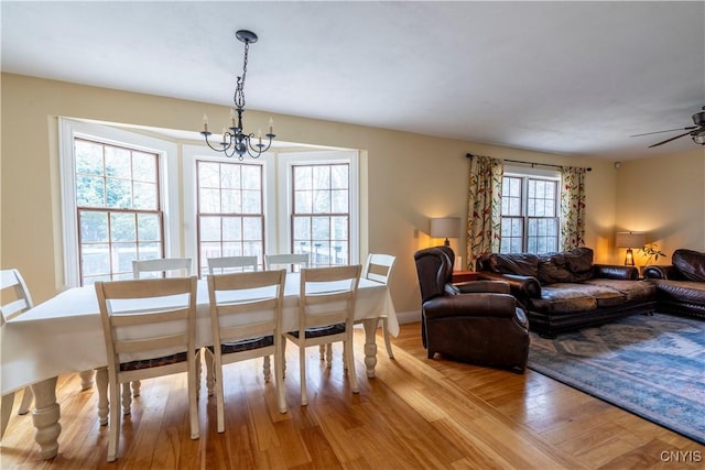 dining space with baseboards, ceiling fan with notable chandelier, and light wood finished floors