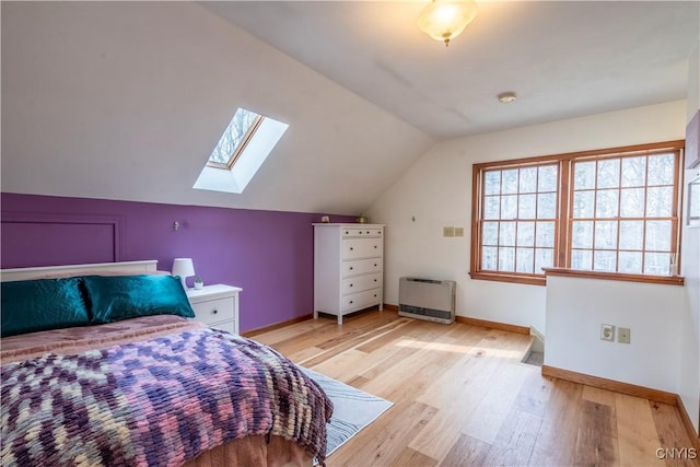 bedroom featuring lofted ceiling with skylight, heating unit, light wood-style floors, and baseboards