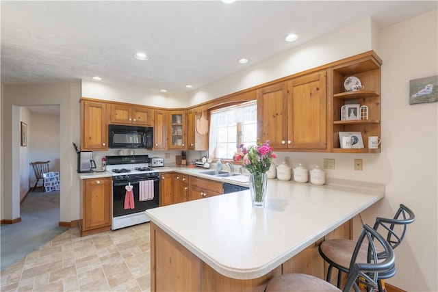 kitchen with a breakfast bar area, brown cabinetry, a peninsula, black microwave, and gas range