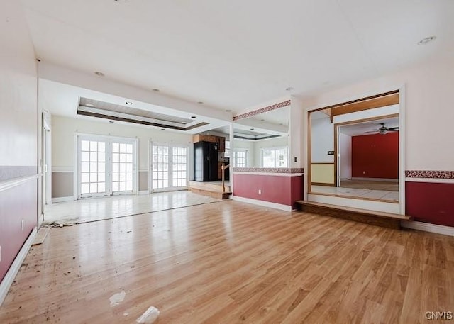 unfurnished living room featuring french doors, a raised ceiling, baseboards, and wood finished floors