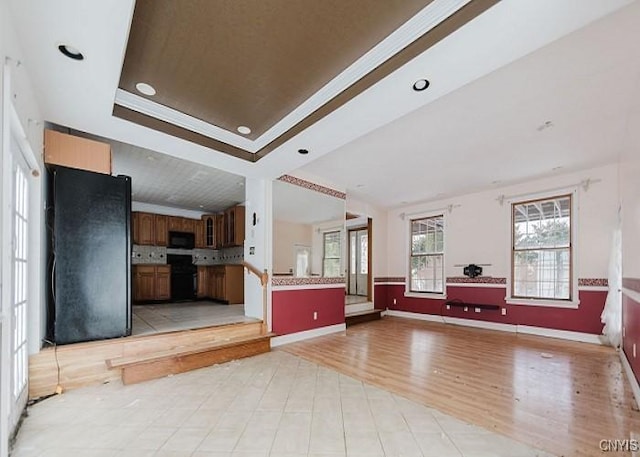 unfurnished living room with a tray ceiling, light wood-style flooring, and baseboards