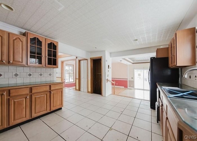 kitchen with light tile patterned floors, glass insert cabinets, tasteful backsplash, and brown cabinets