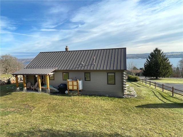 back of house with metal roof, a water view, a yard, and a chimney