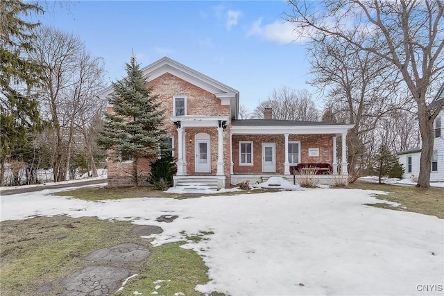 greek revival house featuring covered porch, brick siding, and a chimney