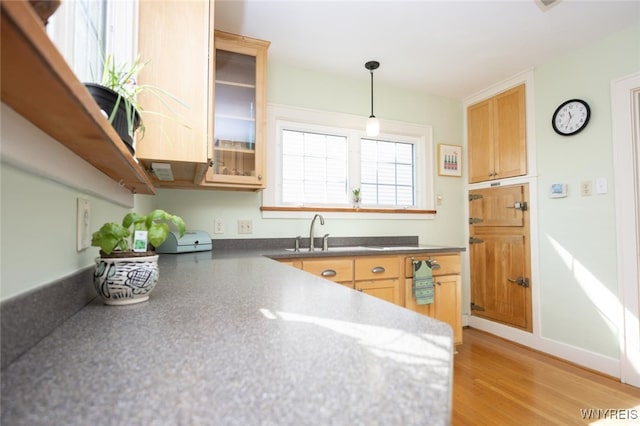 kitchen with glass insert cabinets, light brown cabinetry, light wood-type flooring, hanging light fixtures, and a sink