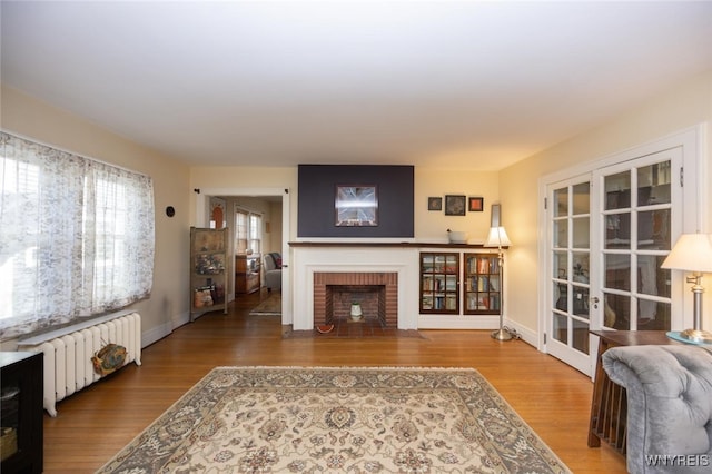 living room featuring a brick fireplace, radiator, wood finished floors, and baseboards