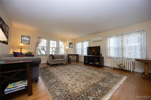 living area featuring a wall unit AC, hardwood / wood-style flooring, radiator heating unit, and baseboards