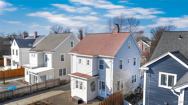 back of property with a residential view, a shingled roof, a chimney, and fence