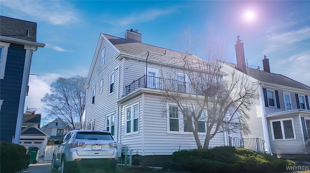 exterior space with a balcony, roof with shingles, and a chimney