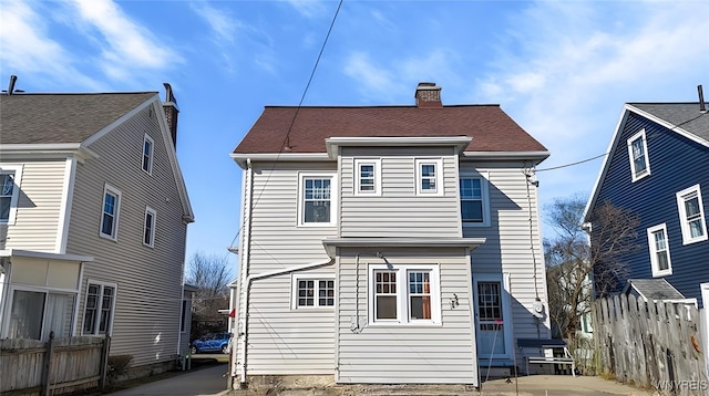 rear view of house featuring a chimney and fence