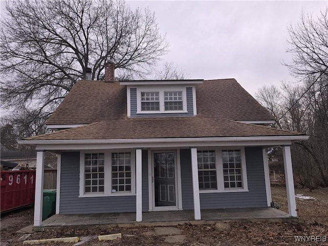 view of front of property with roof with shingles, a porch, a chimney, and fence