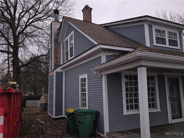 view of home's exterior featuring roof with shingles, a chimney, and fence