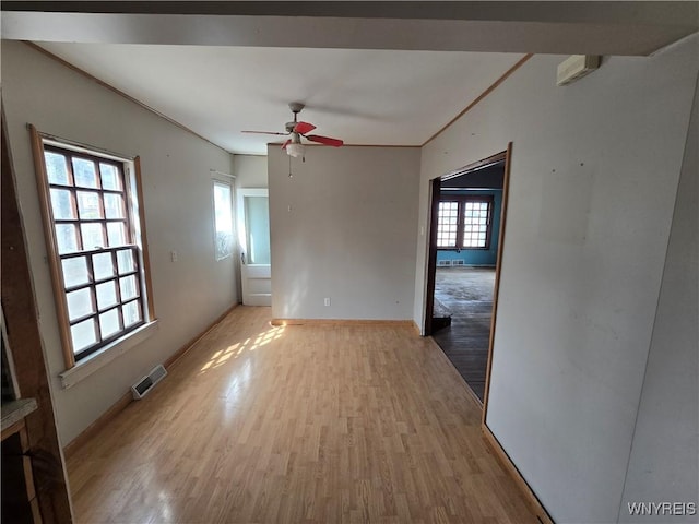 unfurnished room with visible vents, light wood-style flooring, a ceiling fan, and baseboards