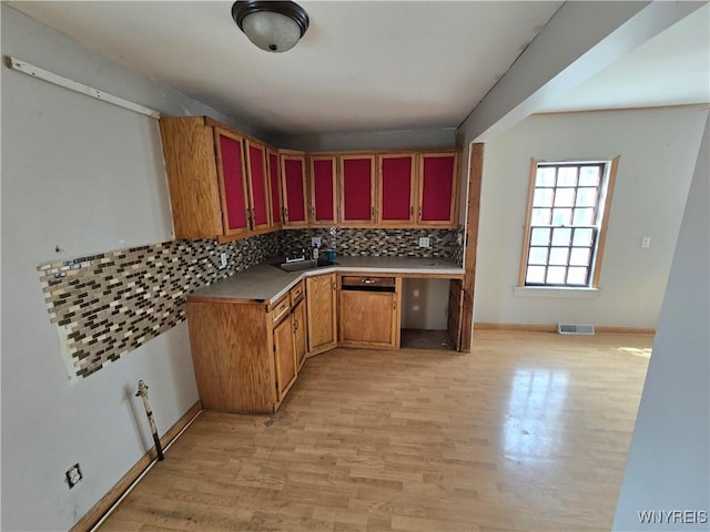 kitchen featuring light wood-type flooring, visible vents, a sink, decorative backsplash, and baseboards