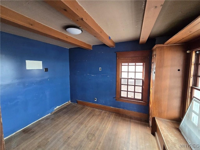 spare room featuring beam ceiling, baseboards, and wood finished floors