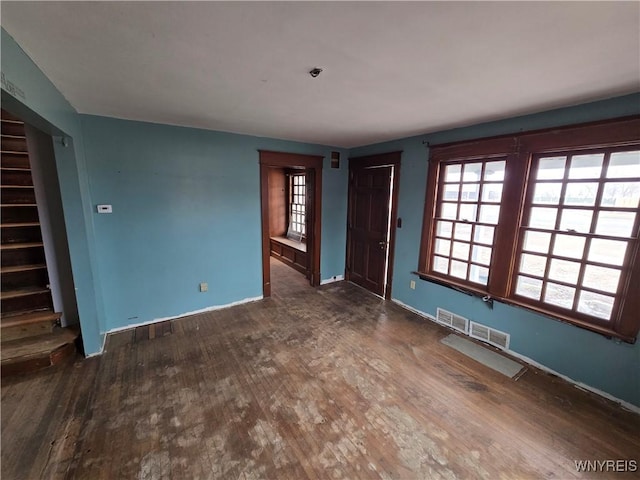 unfurnished living room with visible vents, baseboards, wood finished floors, and stairs