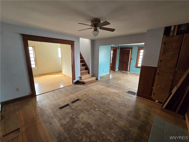 unfurnished living room with stairway, baseboards, visible vents, ceiling fan, and hardwood / wood-style flooring