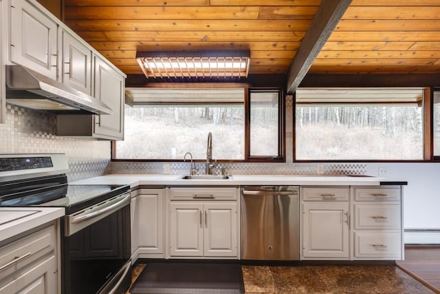 kitchen with a baseboard heating unit, under cabinet range hood, light countertops, appliances with stainless steel finishes, and a sink