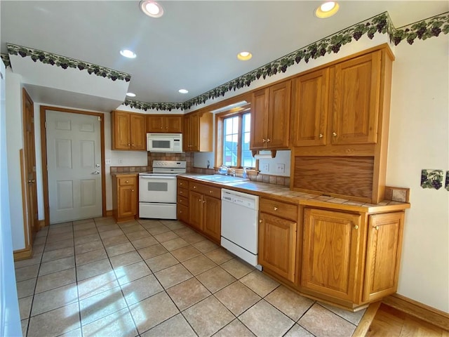 kitchen featuring a sink, tasteful backsplash, recessed lighting, white appliances, and tile counters