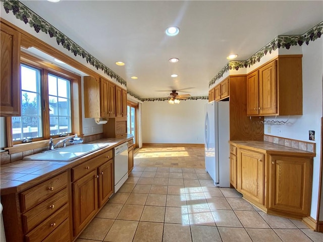 kitchen with a sink, tile countertops, white appliances, light tile patterned floors, and ceiling fan