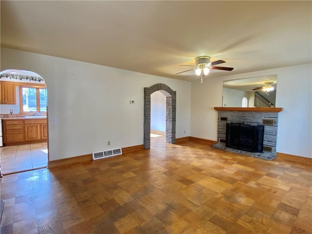 unfurnished living room with baseboards, visible vents, a fireplace with raised hearth, arched walkways, and a sink