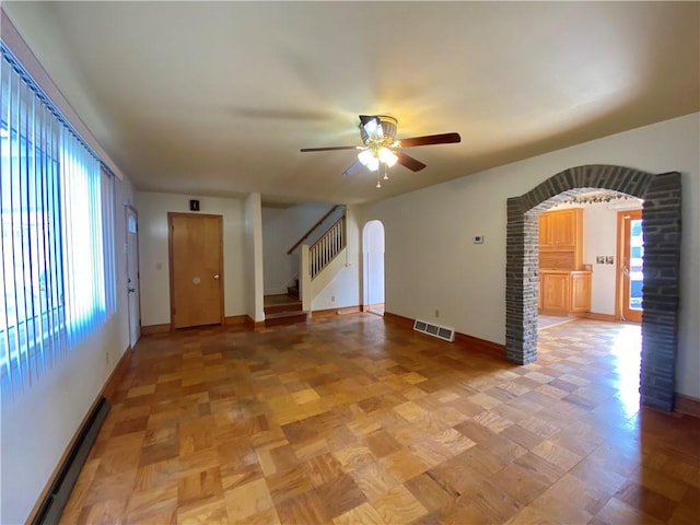 unfurnished living room featuring visible vents, baseboards, stairs, baseboard heating, and arched walkways