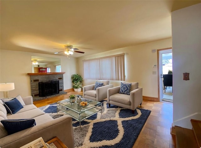 living room with a stone fireplace, a ceiling fan, and baseboards