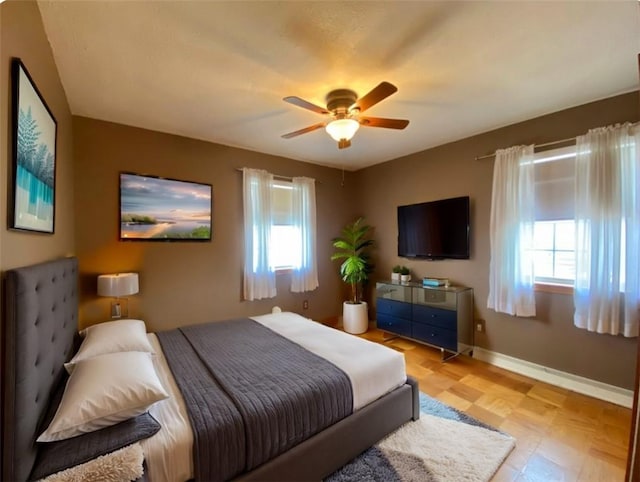 bedroom with multiple windows, light floors, a ceiling fan, and baseboards